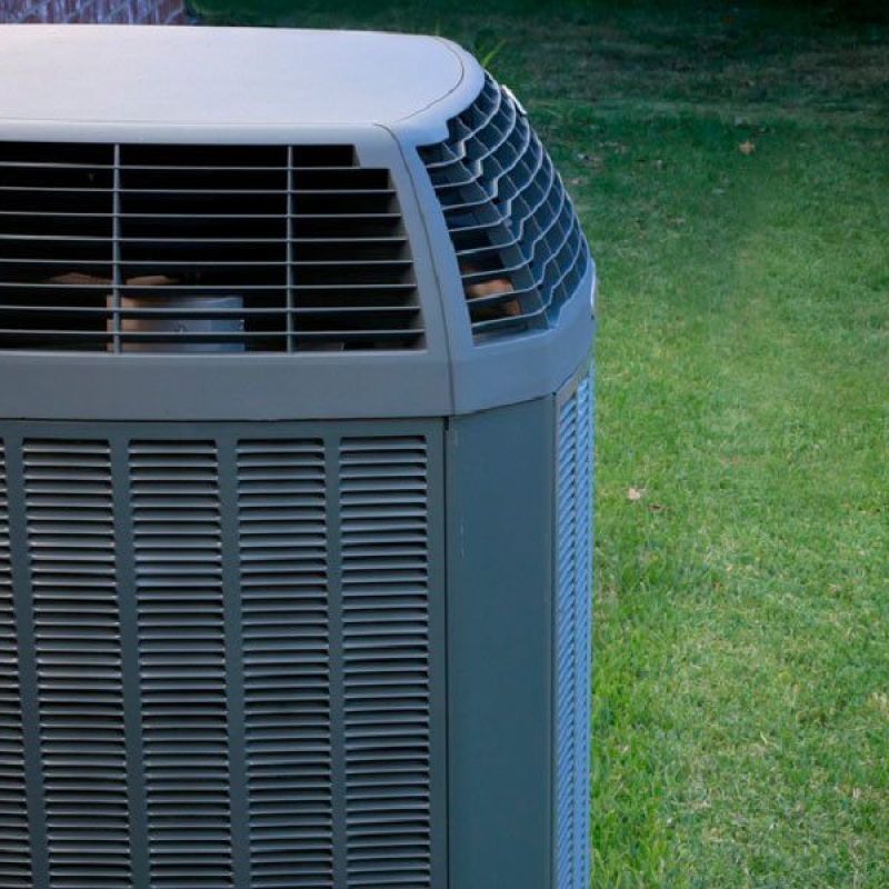 Outdoor air conditioning unit next to a brick wall on a grassy lawn, providing efficient cooling.