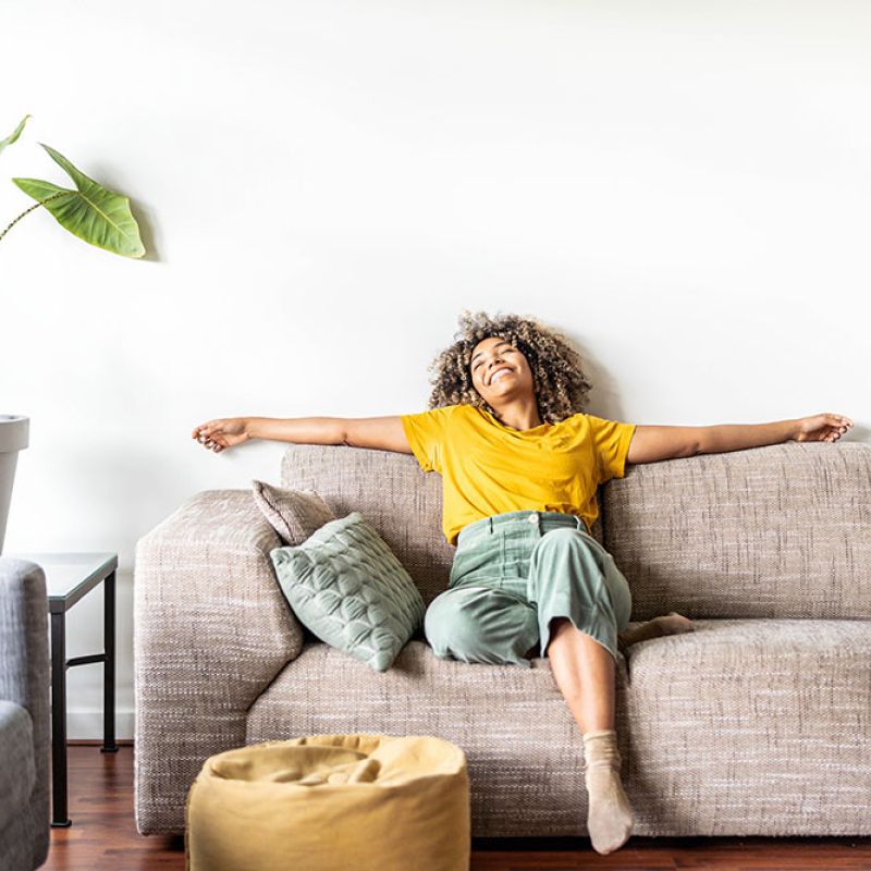 Woman relaxing on a cozy sofa with outstretched arms, joyful and comfortable in a modern living room setting.