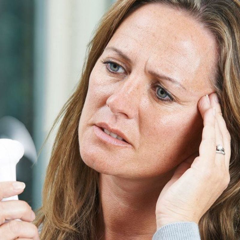 Woman with headache using a portable fan for relief, showing signs of menopause symptoms and discomfort.