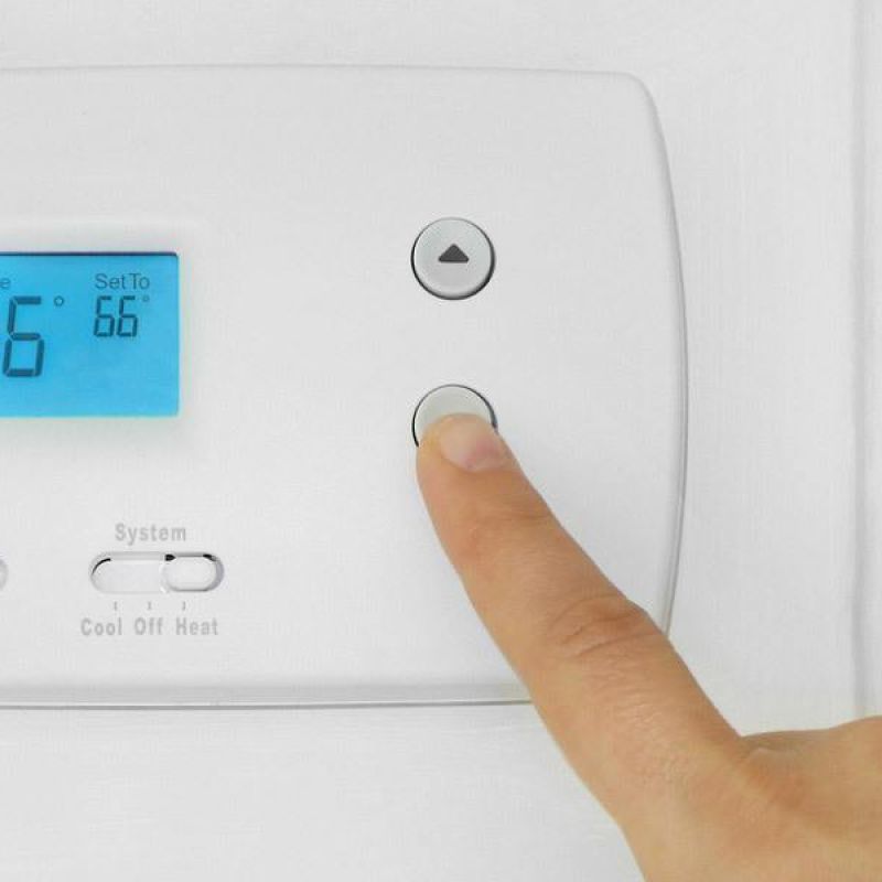 Finger adjusting a digital thermostat to 66 degrees Fahrenheit for home temperature control.