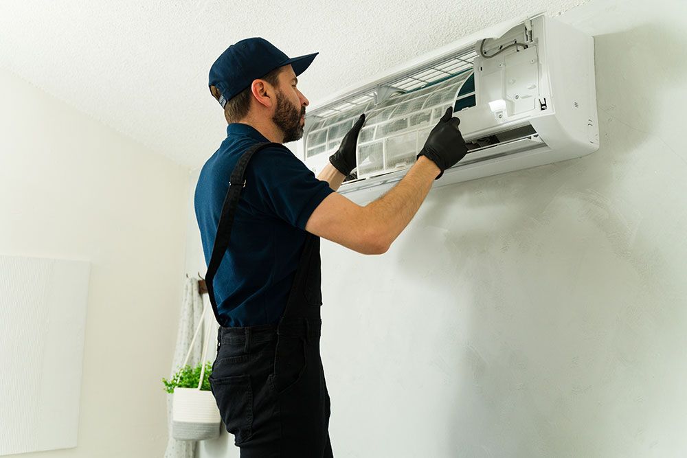 Technician servicing air conditioner filter in a home, wearing gloves and uniform; maintenance and repair concept.