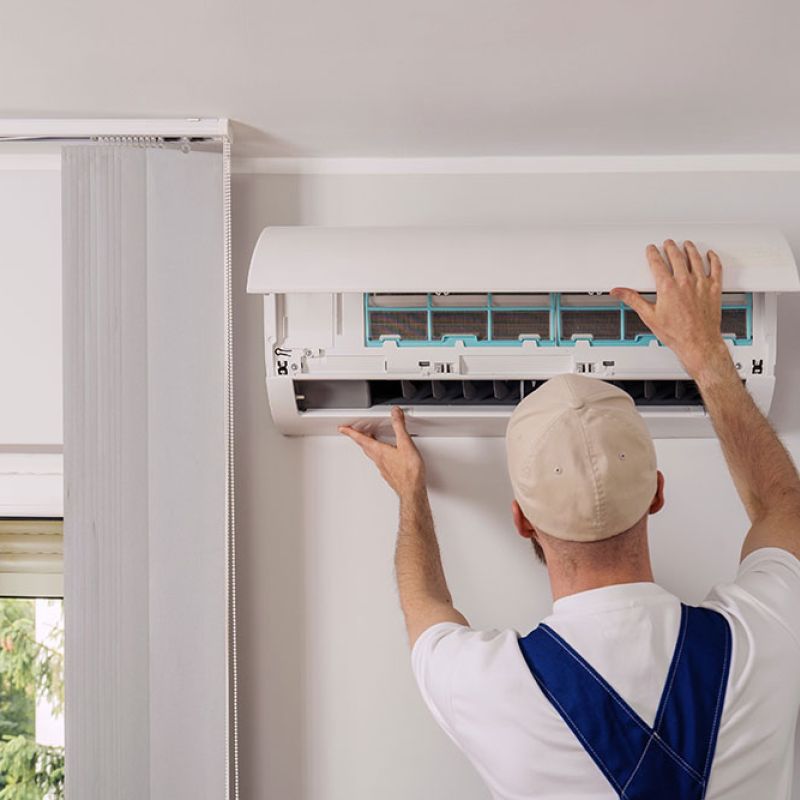 Technician installing or servicing a wall-mounted air conditioning unit inside a modern room.