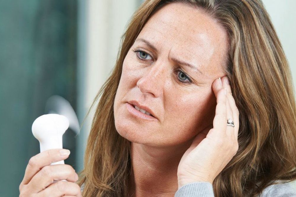 Woman with headache using a portable fan for relief, showing signs of menopause symptoms and discomfort.