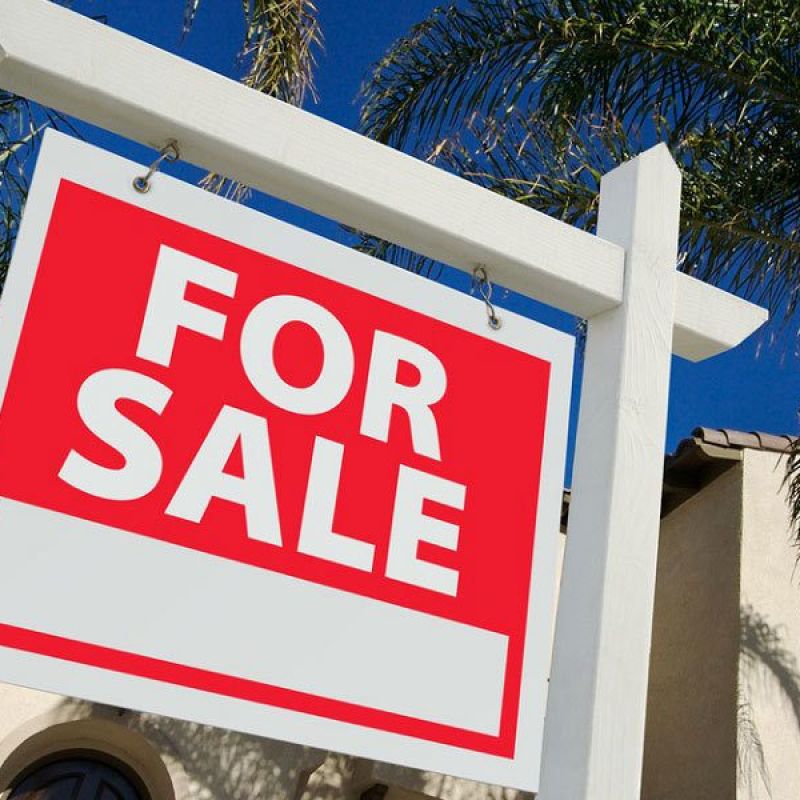 Red For Sale sign in front of a house with palm trees, clear blue sky background. Perfect for real estate listings.