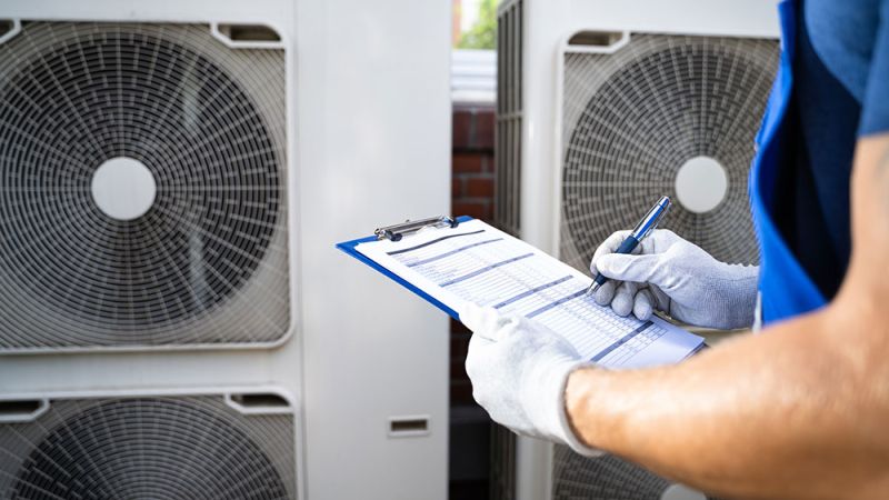 Technician inspecting air conditioning units with a checklist outside a building.