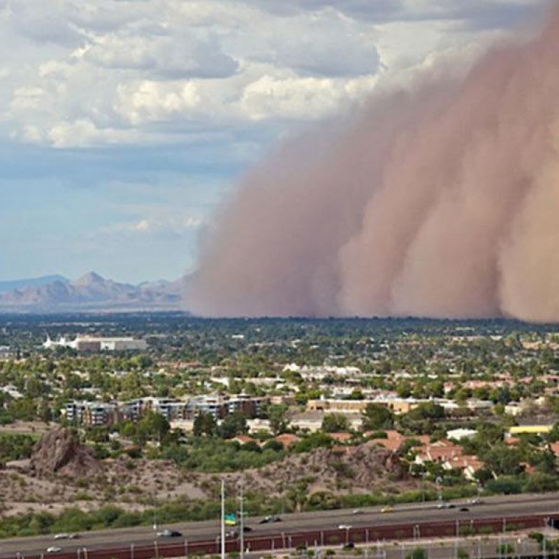 Massive dust storm (haboob) sweeping across a desert city under cloudy skies, with mountains in the background.