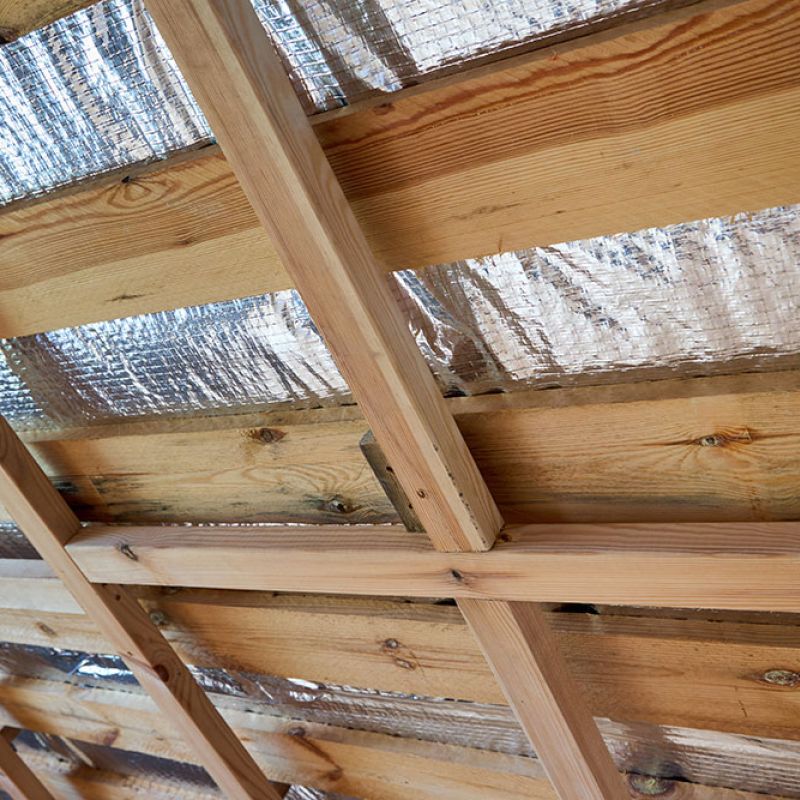 Wooden roof beams with reflective foil insulation for energy efficiency in a home construction project.
