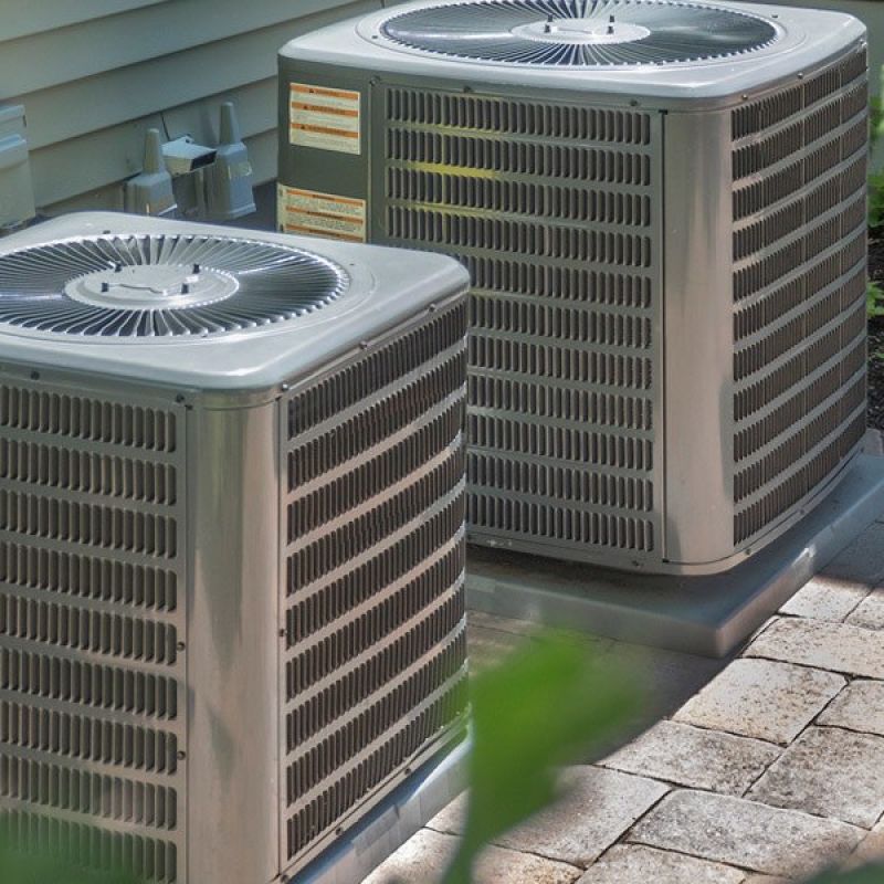 Two outdoor HVAC units on a paved patio, installed for efficient home heating and cooling systems.