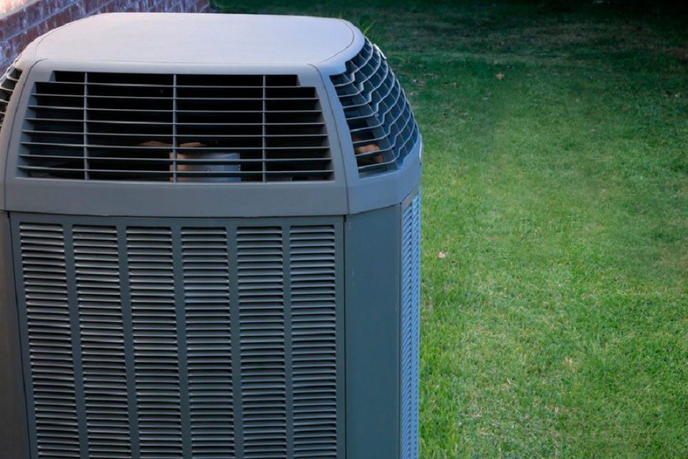 Outdoor air conditioning unit next to a brick wall on a grassy lawn, providing efficient cooling.