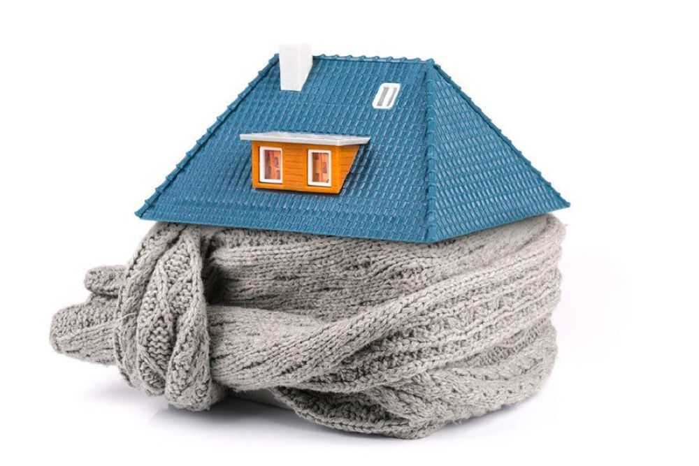House model wrapped in a gray knitted scarf, symbolizing home insulation and energy efficiency.