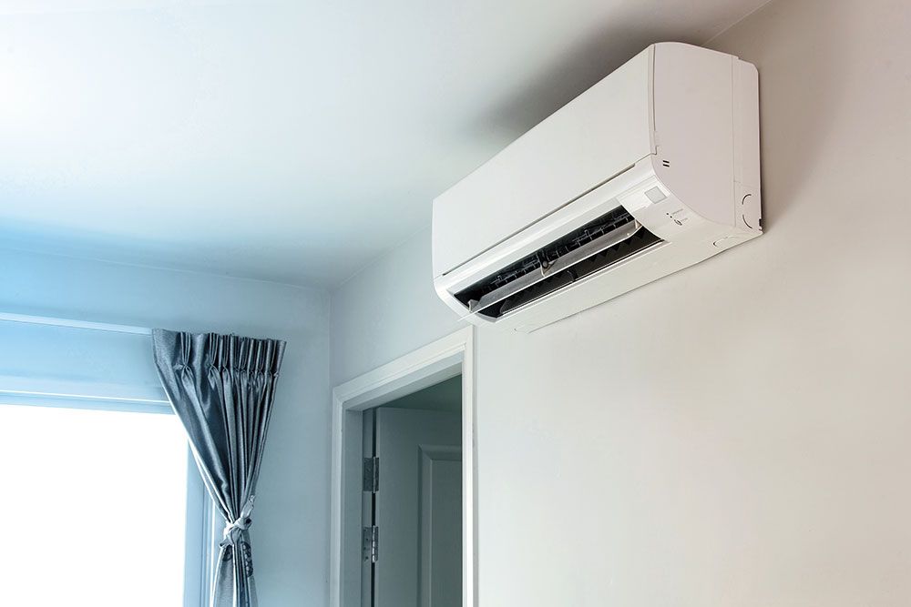 Wall-mounted indoor air conditioner unit in a bright room with a window curtain, offering efficient home cooling.
