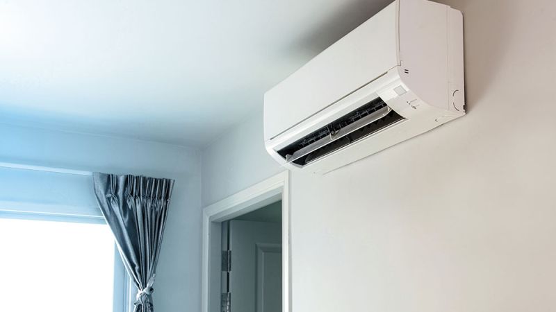 Wall-mounted indoor air conditioner unit in a bright room with a window curtain, offering efficient home cooling.