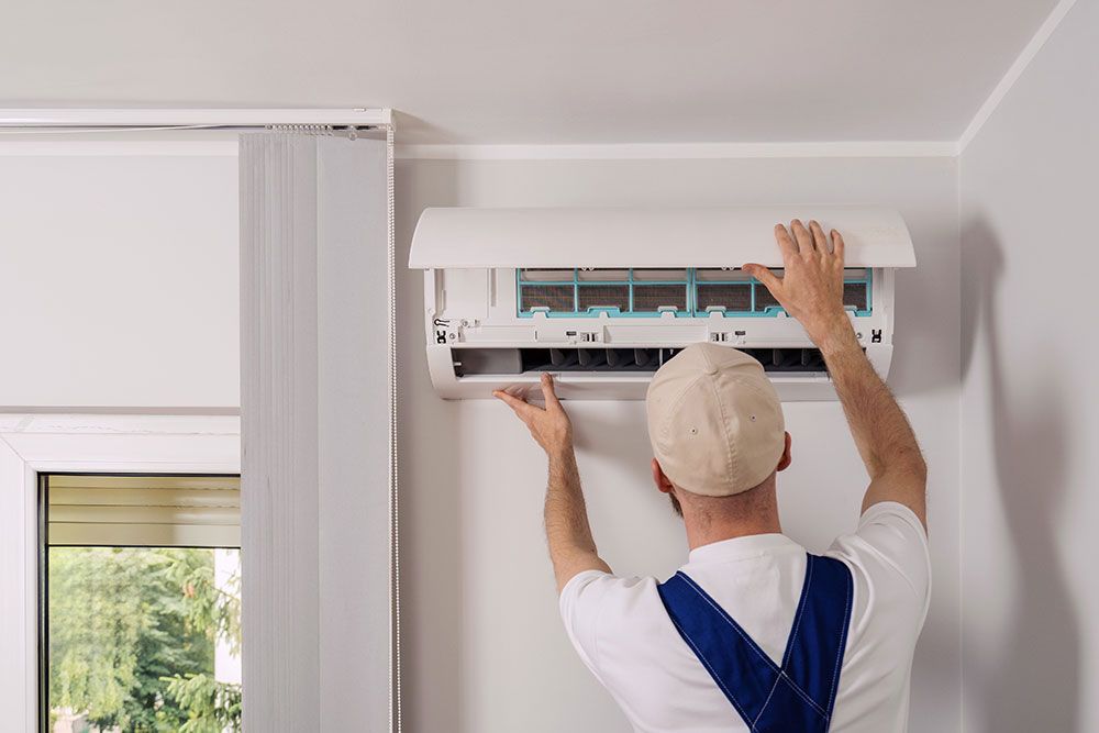 Technician installing or servicing a wall-mounted air conditioning unit inside a modern room.