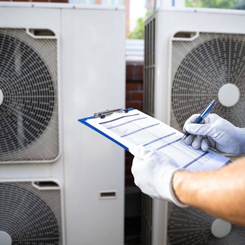 Technician inspecting air conditioning units with a checklist outside a building.