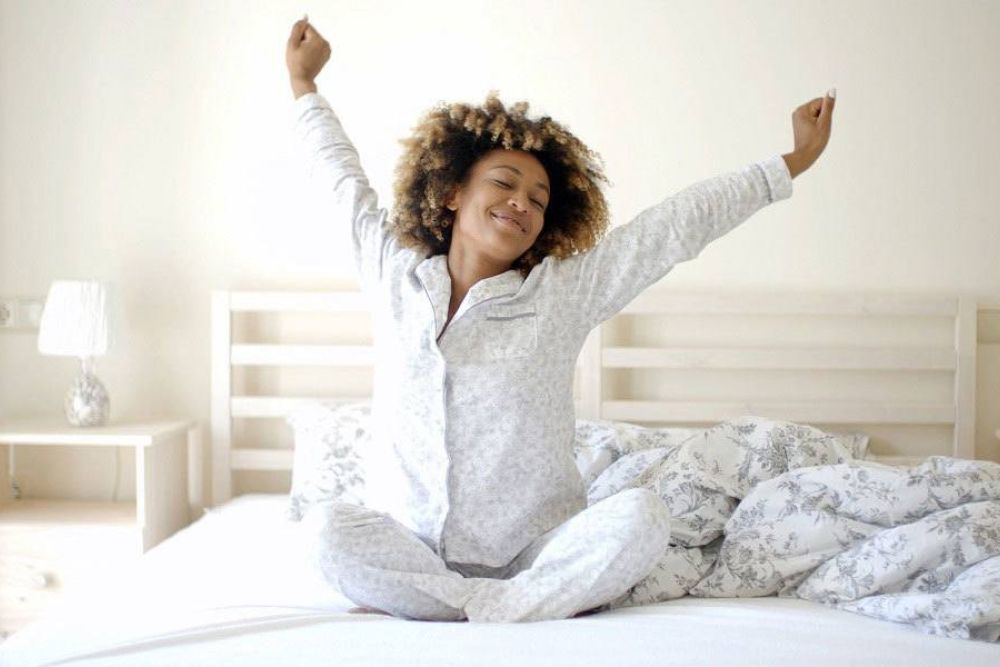 Woman stretching in bed, wearing pajamas, enjoying a fresh morning in a cozy bedroom.