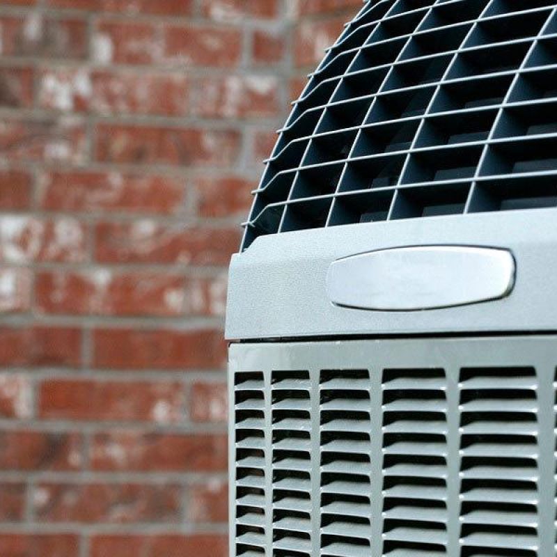 Close-up of an outdoor air conditioning unit against a brick wall, highlighting the vent grille and cooling fins.