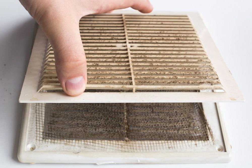 Hand removing dirty air vent cover for cleaning maintenance.