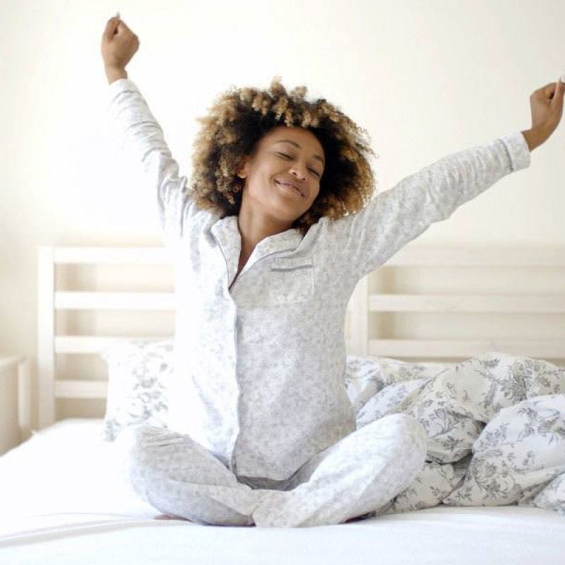Woman stretching in bed, wearing pajamas, enjoying a fresh morning in a cozy bedroom.