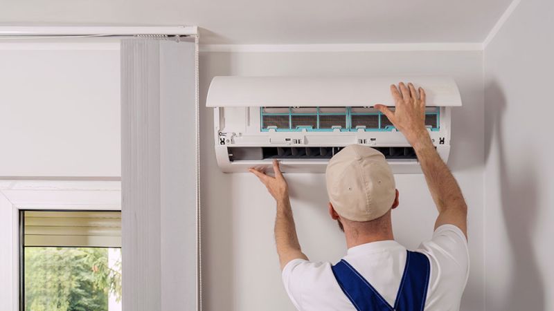 Technician installing or servicing a wall-mounted air conditioning unit inside a modern room.