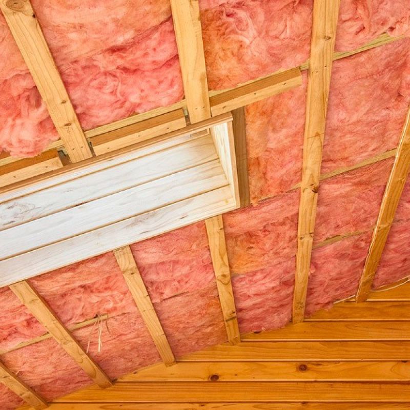 Wooden attic with pink insulation and visible beams, showcasing energy-efficient home improvement techniques.