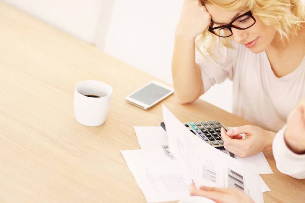 Couple reviewing financial documents with calculator and coffee, focused on budgeting and planning at wooden table.