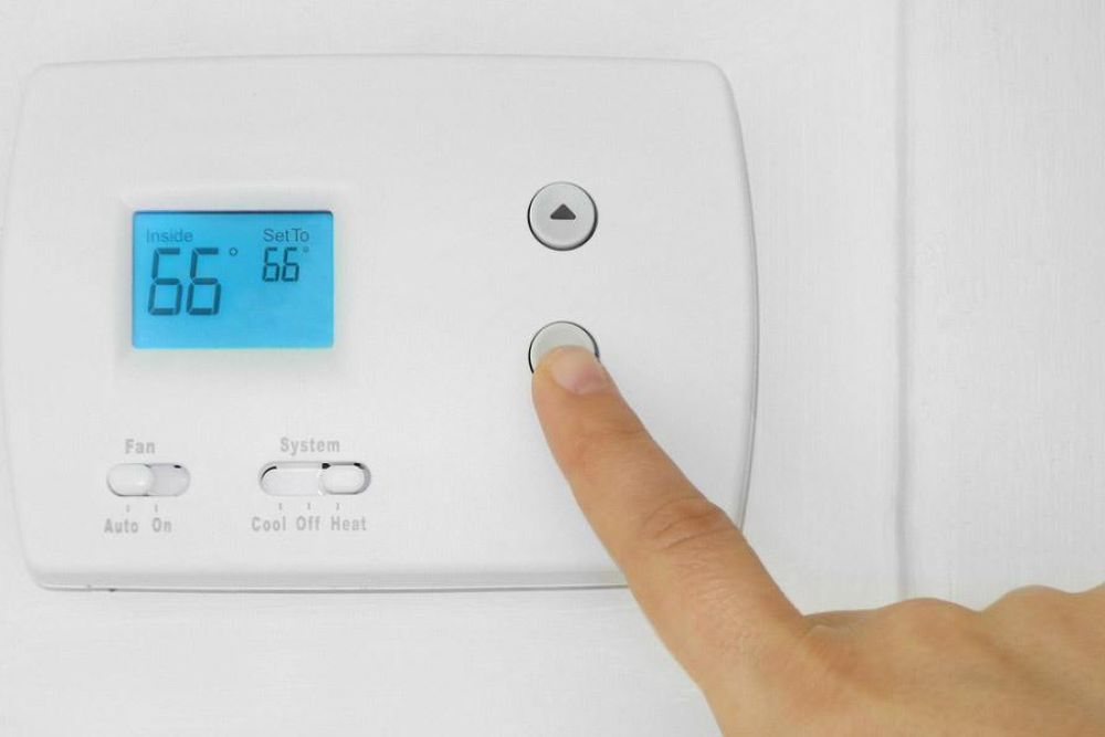 Finger adjusting a digital thermostat to 66 degrees Fahrenheit for home temperature control.