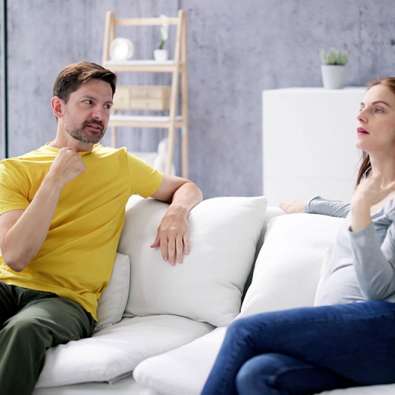 Pregnant woman and man communicating in sign language on a white sofa in a modern living room.
