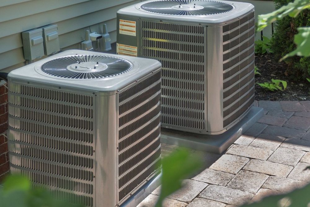 Two outdoor HVAC units on a paved patio, installed for efficient home heating and cooling systems.