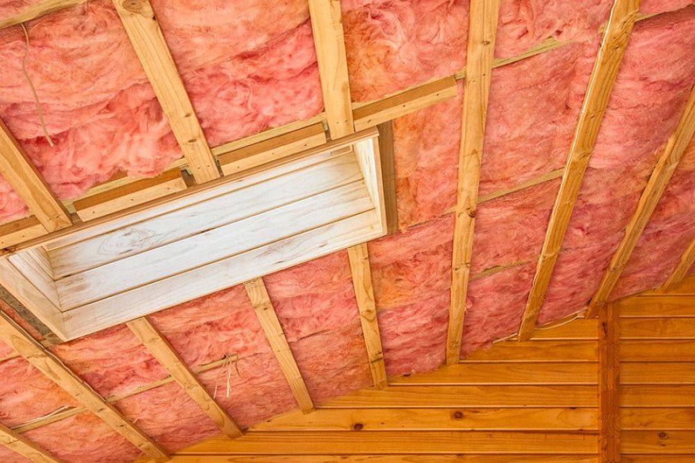 Wooden attic with pink insulation and visible beams, showcasing energy-efficient home improvement techniques.
