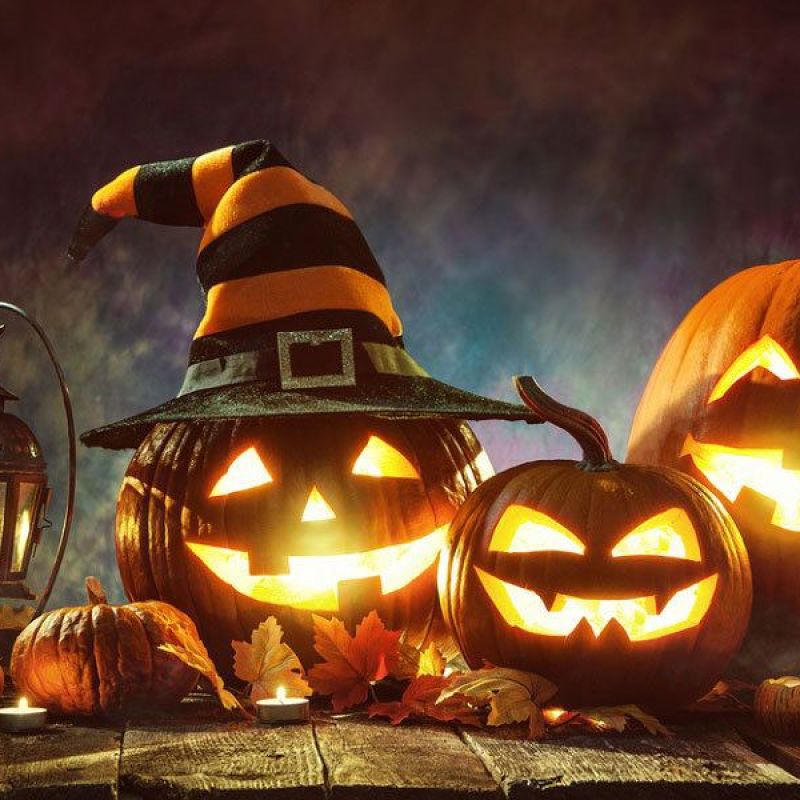 Halloween scene with glowing jack-o'-lanterns, witch hat, autumn leaves, and lantern for a spooky festive vibe.