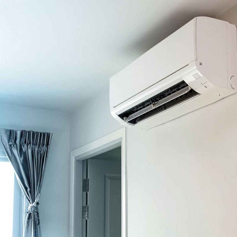 Wall-mounted indoor air conditioner unit in a bright room with a window curtain, offering efficient home cooling.