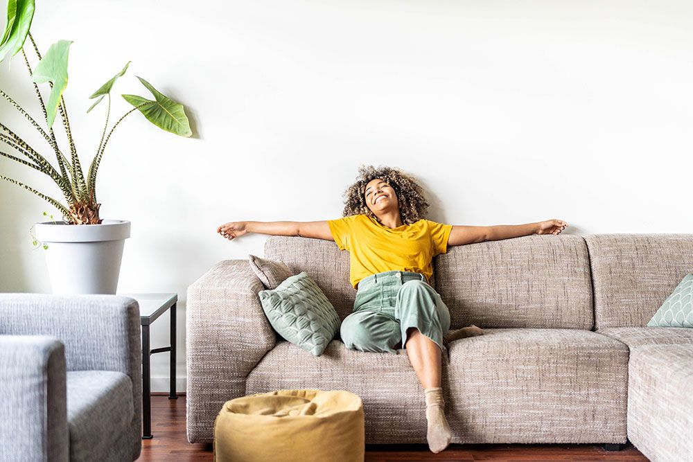 Woman relaxing on a cozy sofa with outstretched arms, joyful and comfortable in a modern living room setting.