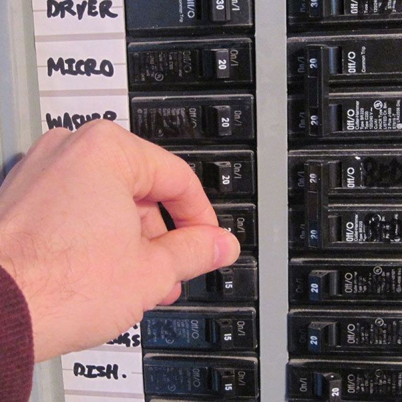 Hand switches off circuit breaker in labeled electrical panel.