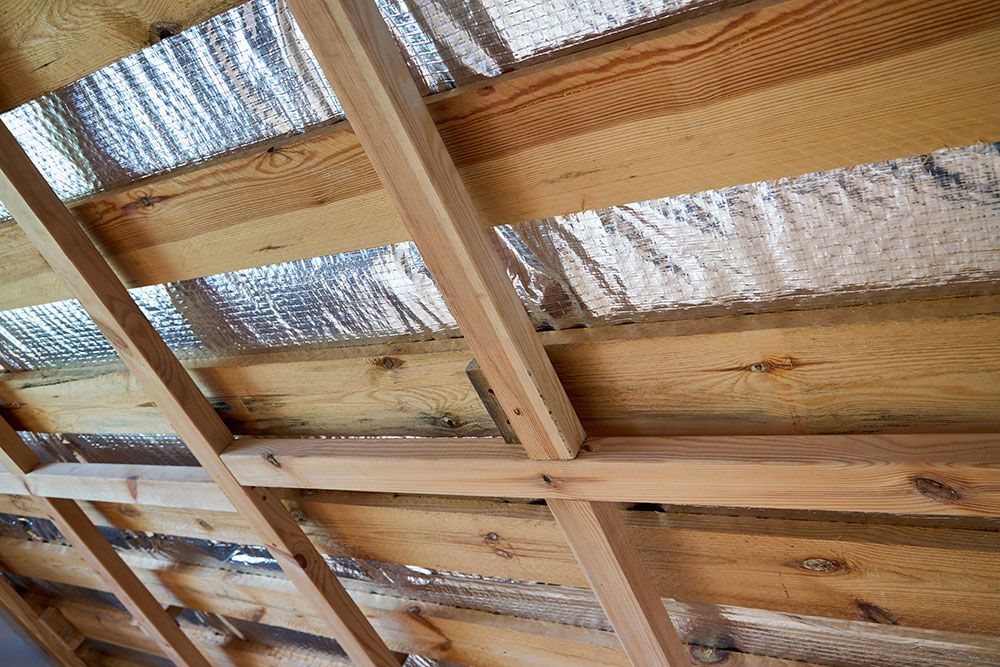 Wooden roof beams with reflective foil insulation for energy efficiency in a home construction project.