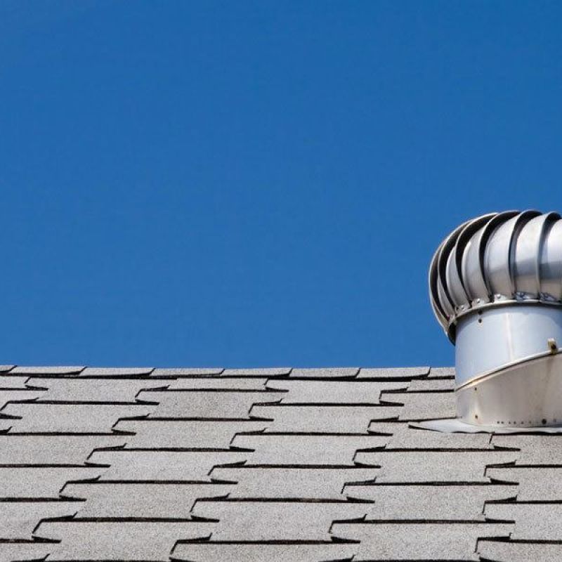 Modern gray roof with a spinning vent turbine under a clear blue sky, showcasing efficient attic ventilation.