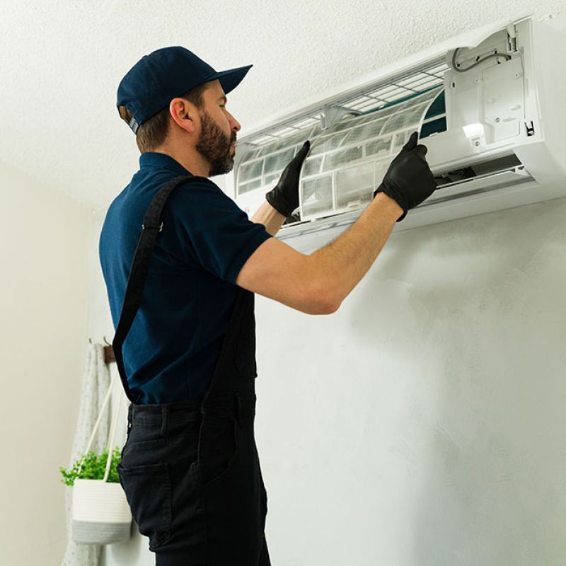 Technician servicing air conditioner filter in a home, wearing gloves and uniform; maintenance and repair concept.