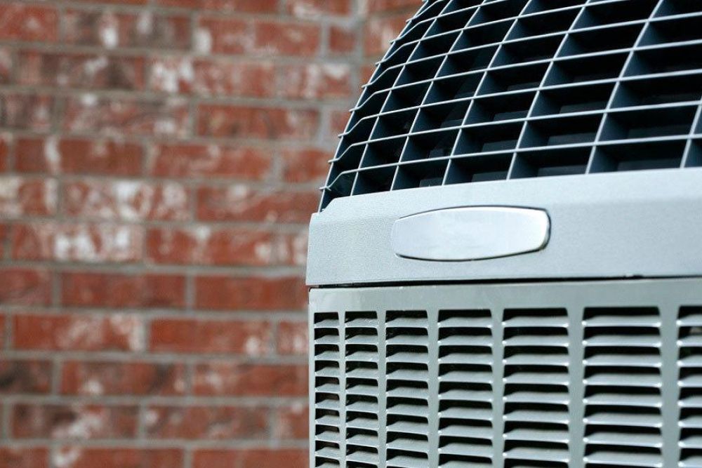 Close-up of an outdoor air conditioning unit against a brick wall, highlighting the vent grille and cooling fins.