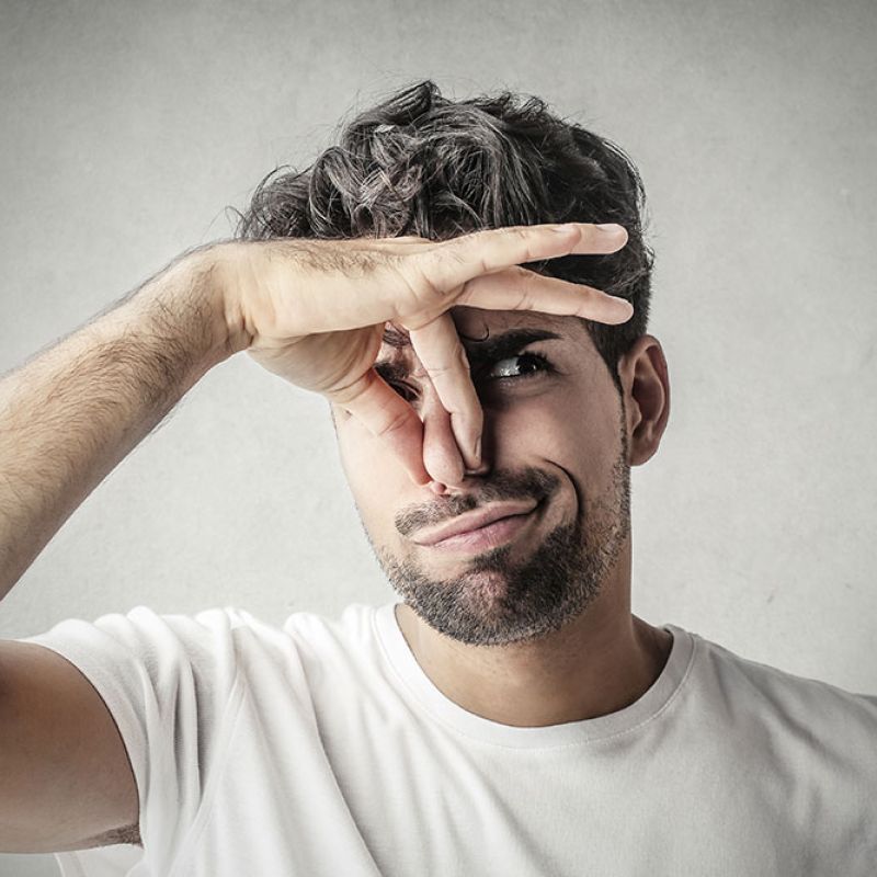 Man in white shirt pinching nose, expressing disgust or bad smell against gray background.